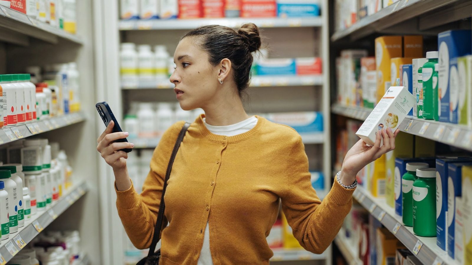 Shopper comparing a supplement box against her scanner app in a pharmacy aisle