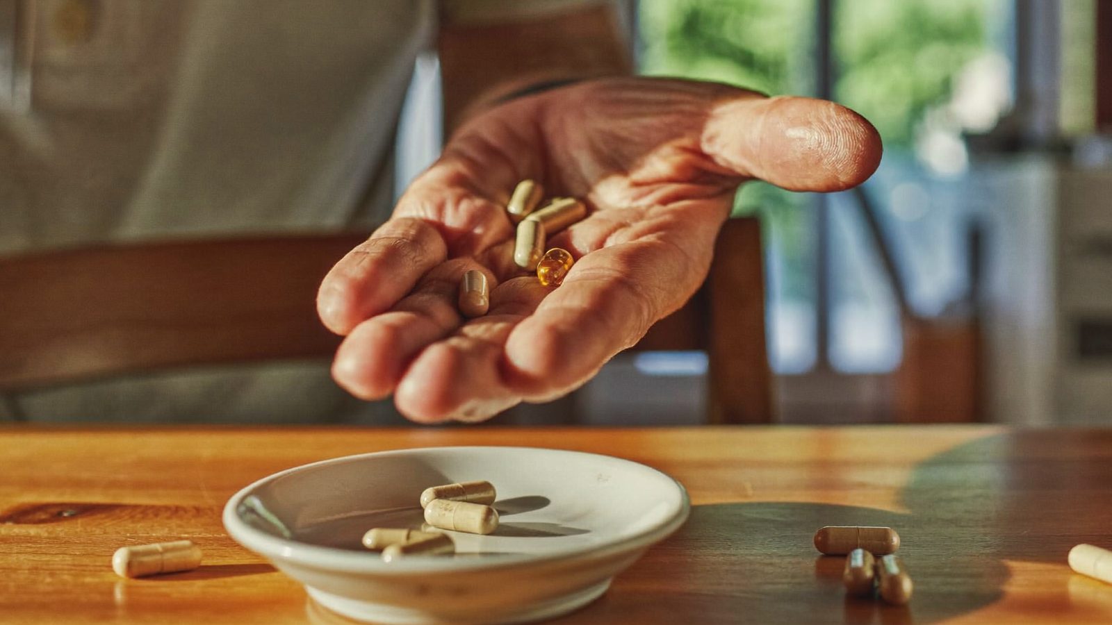 Loose supplement capsules in an open palm above a small dish