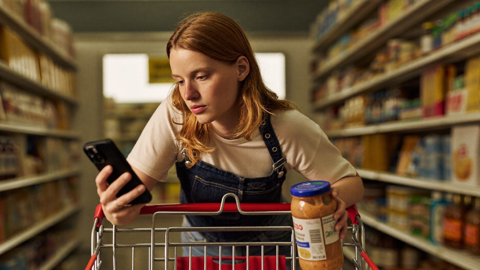Shopper checking a scanner app while deciding on a jar in the grocery aisle